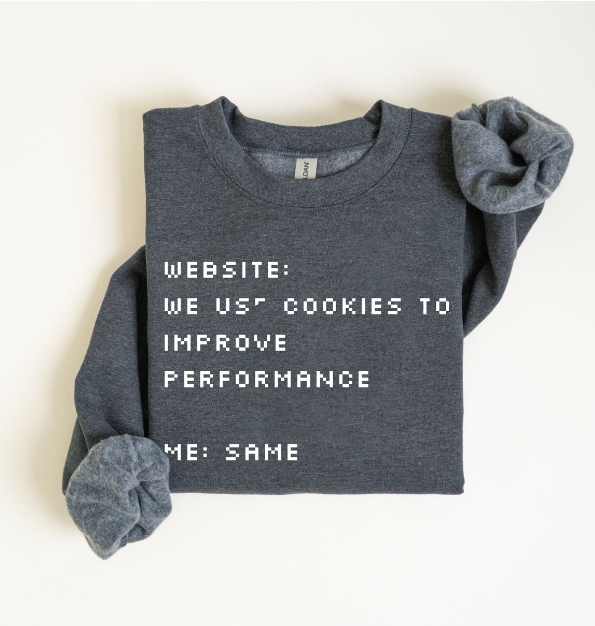 A folded dark heather gray sweatshirt with white pixel-style text reading 'WEBSITE: WE US* COOKIES TO IMPROVE PERFORMANCE' and 'ME: SAME', shown on a plain light background.