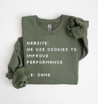 An olive green crewneck sweatshirt with a long sleeve folded over, featuring pixel-style white text that reads 'WEBSITE: WE USE COOKIES TO IMPROVE PERFORMANCE' and 'E: SAME'. A matching scrunchie is placed on the right shoulder.
