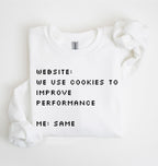A white crewneck sweatshirt with black pixel-style text reading 'WEBSITE: WE USE COOKIES TO IMPROVE PERFORMANCE ME: SAME', shown folded on a white background with a matching white fabric prop near the shoulder.