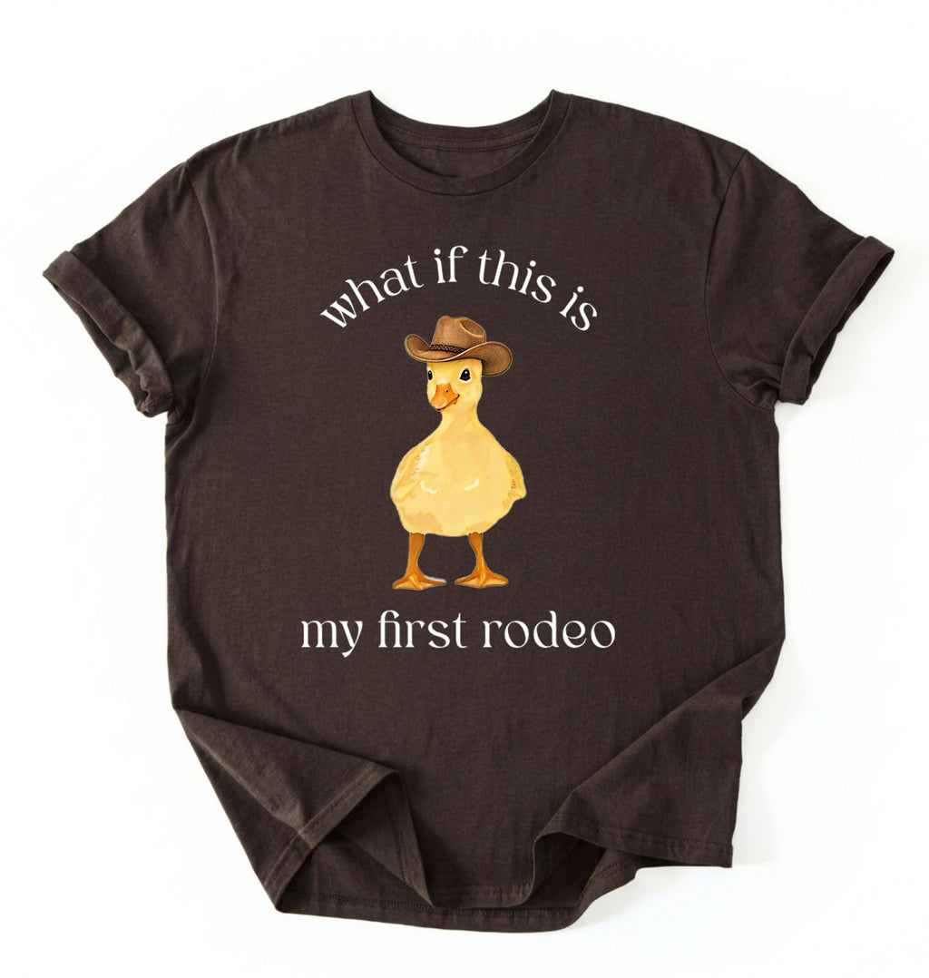 Flat lay of a dark chocolate what if this is my first rodeo shirt brown funny cowboy duck t shirt western humor gift on a white background 