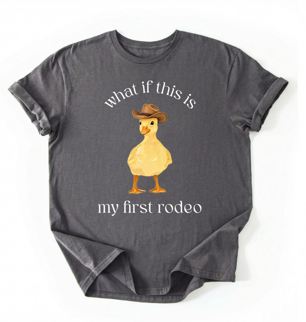 Flat lay of a pepper what if this is my first rodeo shirt brown funny cowboy duck t shirt western humor gift on a white background 