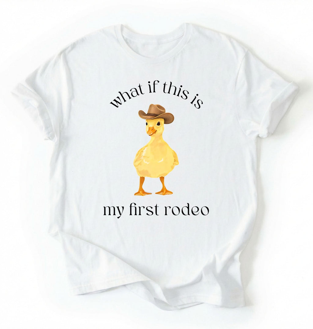 Flat lay of a White what if this is my first rodeo shirt brown funny cowboy duck t shirt western humor gift on a white background 