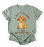 Flat lay of a bay whimsical frog shirt cream cute mushroom frog t shirt cottagecore aesthetic gift design on a white background 