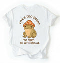 Flat lay of a white whimsical frog shirt cream cute mushroom frog t shirt cottagecore aesthetic gift design on a white background 