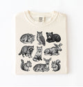 Ivory t-shirt featuring detailed woodland animal illustrations including deer, fox, bear, owl, and raccoon