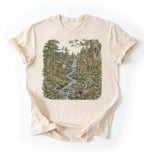 Flat lay of a natural Woodland forest animals shirt featuring deer, raccoons, and scenic nature illustration on a white background 