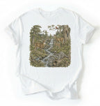 Flat lay of a white Woodland forest animals shirt featuring deer, raccoons, and scenic nature illustration on a white background 