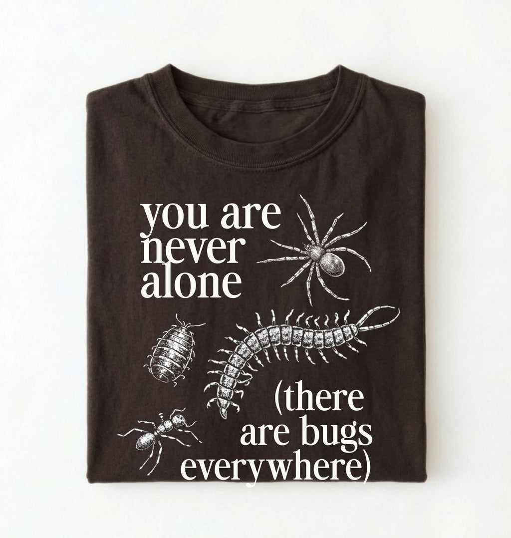 Flat lay of a darkchocolate t-shirt featuring illustrated insects including a spider and centipede with text reading “You Are Never Alone (there are bugs everywhere). Funny bug shirt insect illustrations design perfect gift for science lovers 
