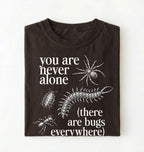 Flat lay of a darkchocolate t-shirt featuring illustrated insects including a spider and centipede with text reading “You Are Never Alone (there are bugs everywhere). Funny bug shirt insect illustrations design perfect gift for science lovers 