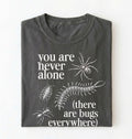 Flat lay of a pepper t-shirt featuring illustrated insects including a spider and centipede with text reading “You Are Never Alone (there are bugs everywhere). Funny bug shirt insect illustrations design perfect gift for science lovers 