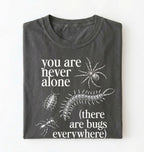 Flat lay of a pepper t-shirt featuring illustrated insects including a spider and centipede with text reading “You Are Never Alone (there are bugs everywhere). Funny bug shirt insect illustrations design perfect gift for science lovers 